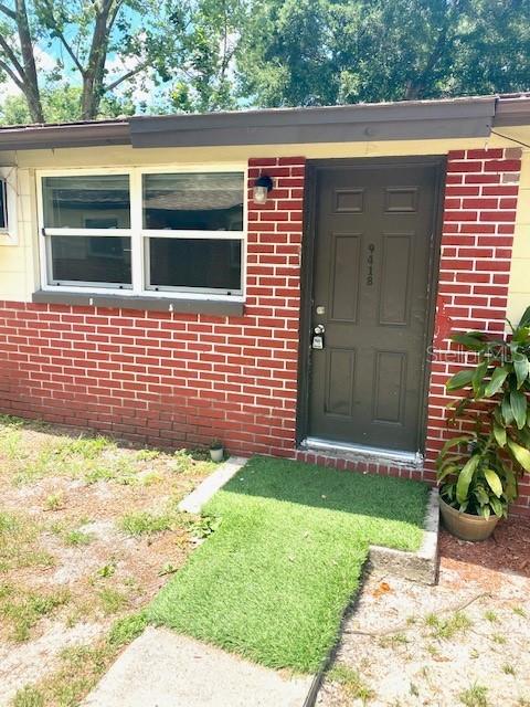 A brick exterior wall features a dark front door and a white-framed window — 9418 GREYSTONE ROAD, THONOTOSASSA, FL