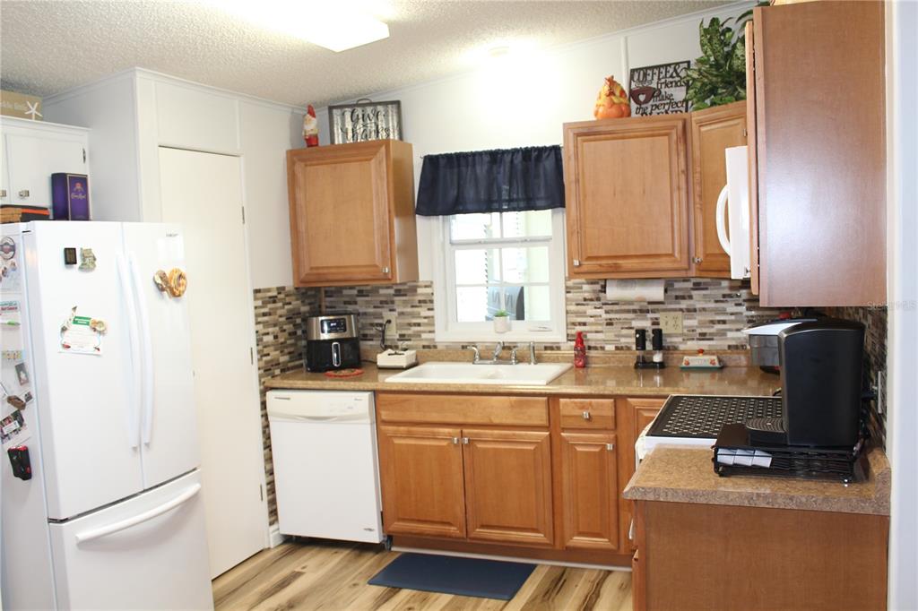 A kitchen with wood cabinets, a white dishwasher, a tiled backsplash, and a window — 4415 14TH STREET E, ELLENTON, FL