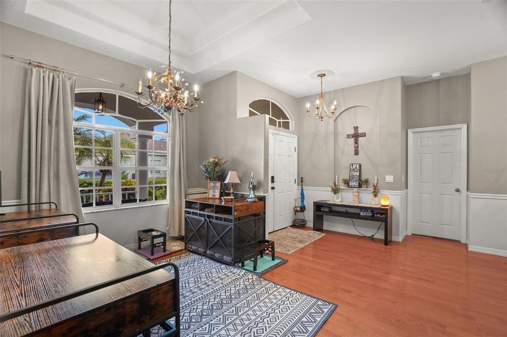 A bright foyer features hardwood floors, a patterned rug, two chandeliers, and a wooden console — 2117 LARKSPUR COURT, TRINITY, FL
