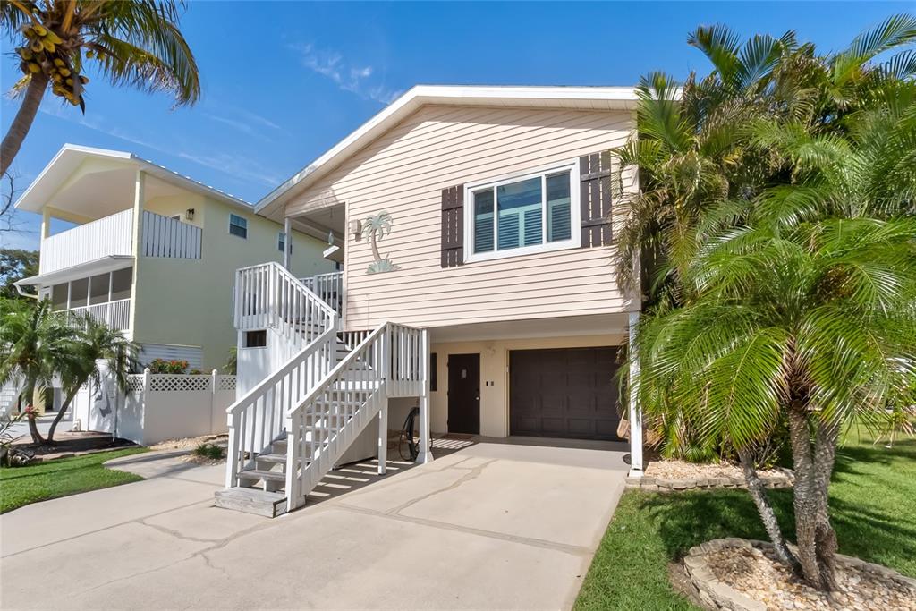 An elevated house with light siding, a white staircase, a garage, and surrounding palm trees — 2905 AVENUE C, HOLMES BEACH, FL