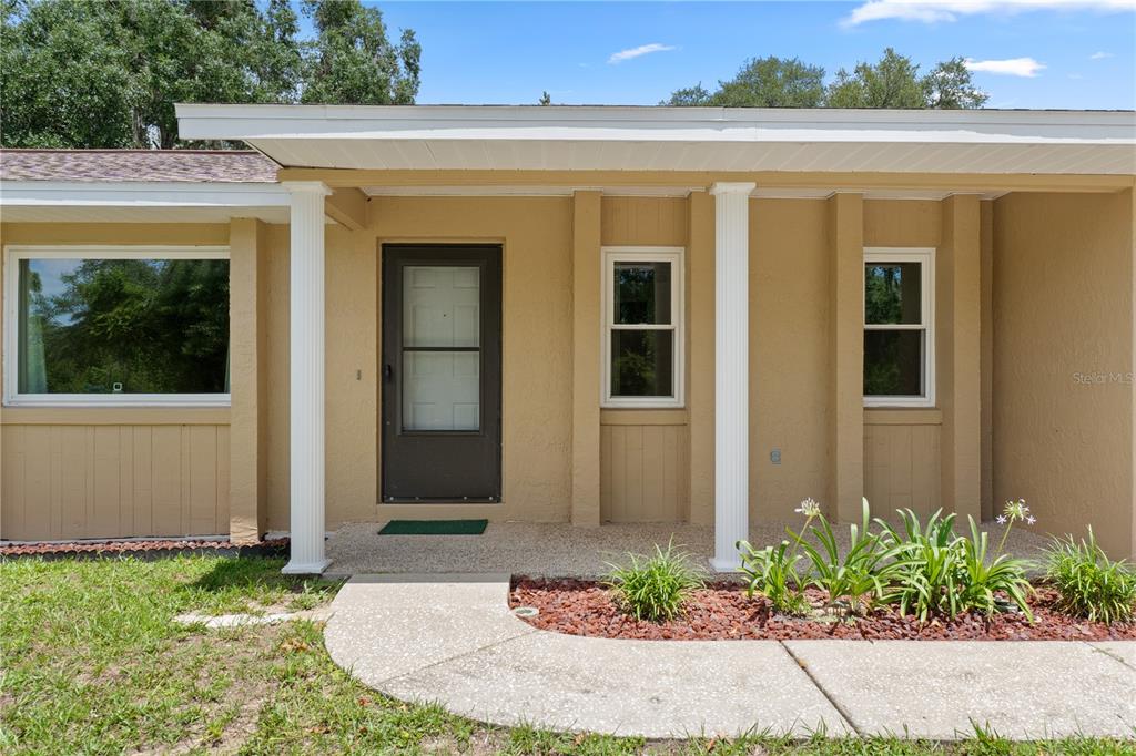 The exterior of a tan house features a covered porch, a front door, and windows — 9390 E WINDWOOD LOOP, INVERNESS, FL