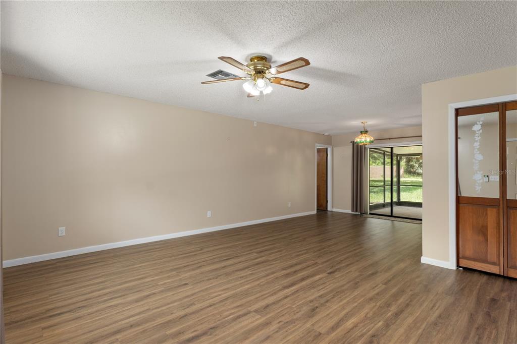 A spacious living room features wood-look flooring, a ceiling fan, and sliding glass patio doors — 9390 E WINDWOOD LOOP, INVERNESS, FL