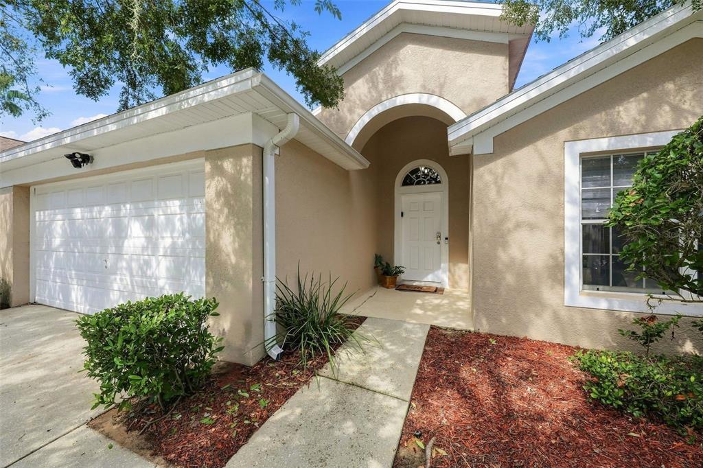 A beige house exterior features a white garage door, a front entrance, and landscaped mulch — 510 CASTLEMAIN CIRCLE, DAVENPORT, FL