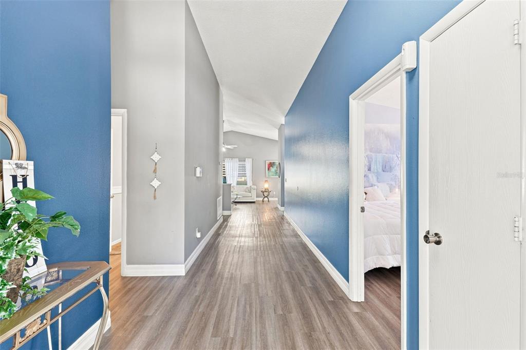 A hallway with blue and gray walls leads to a living area with wood-look flooring — 510 CASTLEMAIN CIRCLE, DAVENPORT, FL