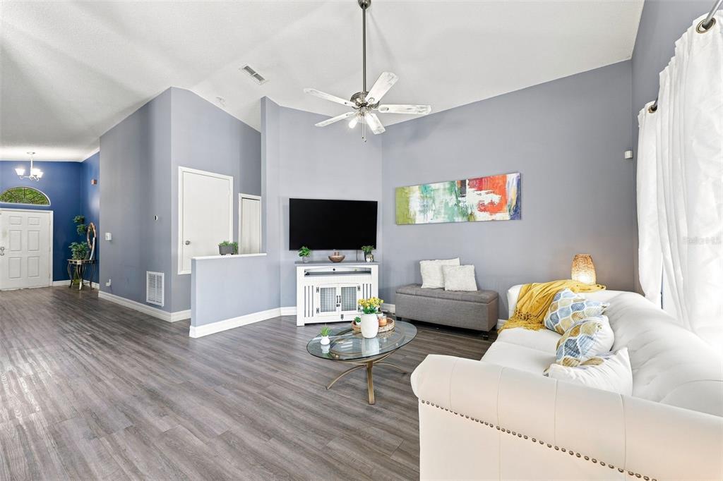 A living room features gray walls, wood-look flooring, a white sofa, and a ceiling fan — 510 CASTLEMAIN CIRCLE, DAVENPORT, FL