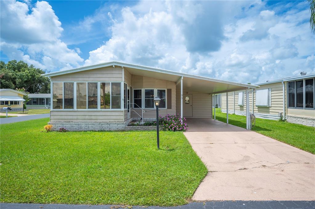 A single-story manufactured home with a sunroom, carport, and a grassy front yard — 95 PARSON DRIVE, WINTER HAVEN, FL
