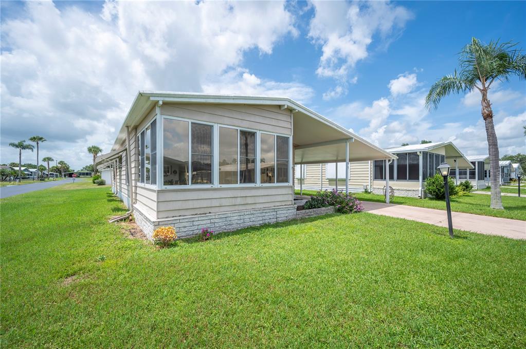 A beige mobile home with a screened-in porch and a carport sits on a lawn — 95 PARSON DRIVE, WINTER HAVEN, FL