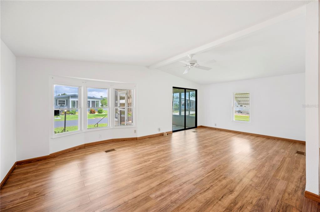 An empty living room with wood-look flooring, a ceiling fan, and large windows — 95 PARSON DRIVE, WINTER HAVEN, FL
