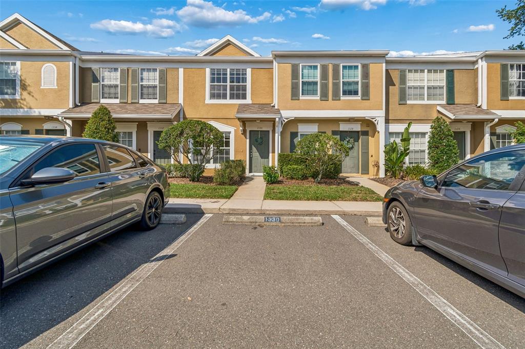 A row of two-story townhomes with tan stucco exteriors and assigned parking spaces in front — 1330 STANDRIDGE DRIVE, WESLEY CHAPEL, FL