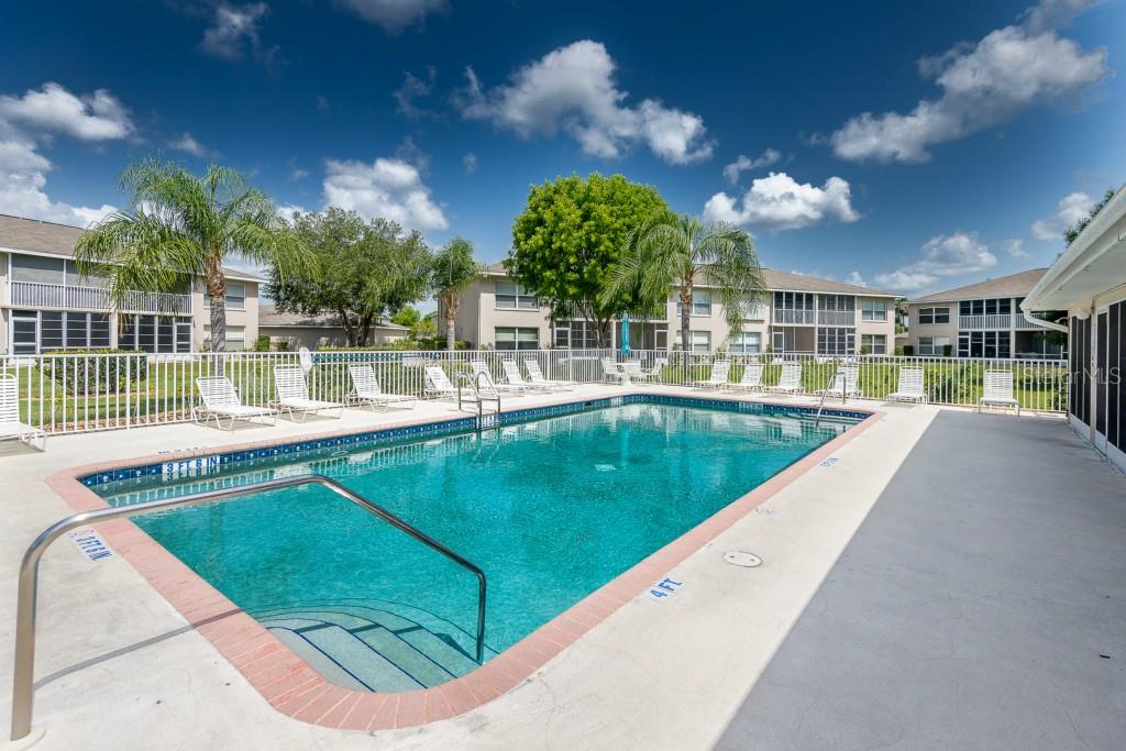 An outdoor swimming pool with a shallow entry area surrounded by lounge chairs and buildings — 11644 EGRET CIRCLE UNIT 1101, LAKE SUZY, FL