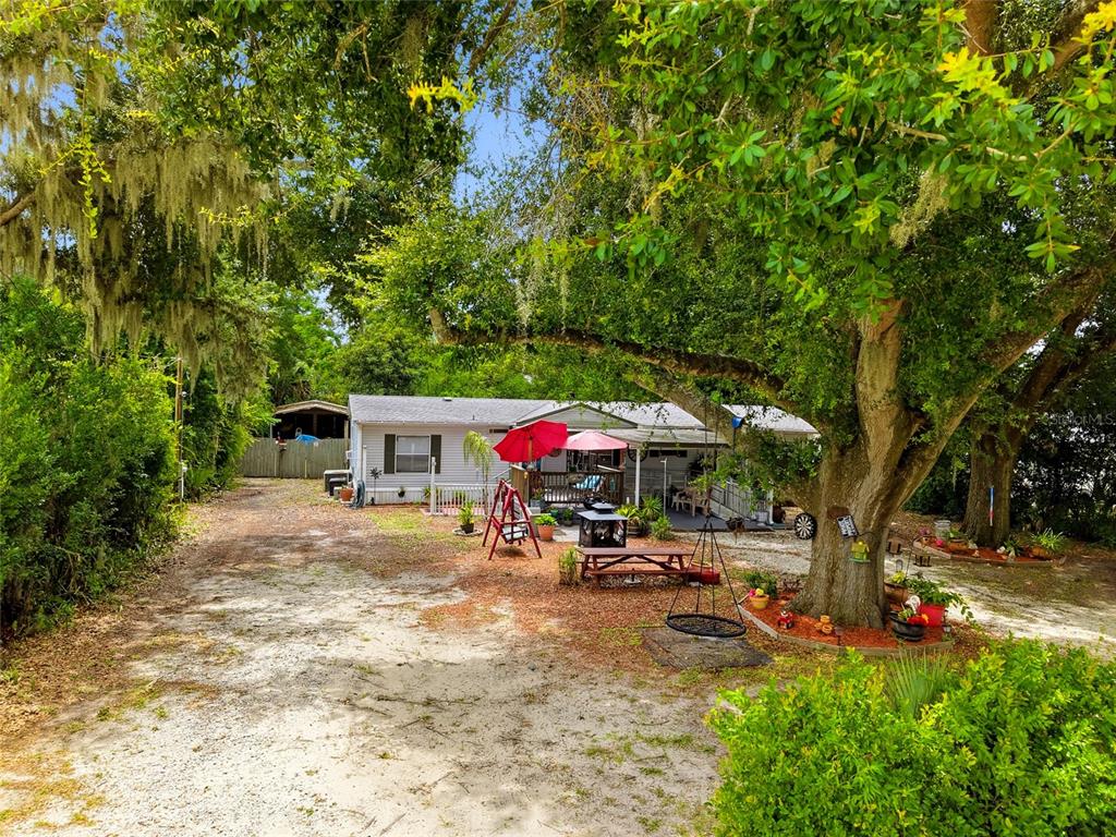 A single-story house with a gravel driveway, a large oak tree, and a patio area — 29514 BENJAMIN DRIVE, WESLEY CHAPEL, FL