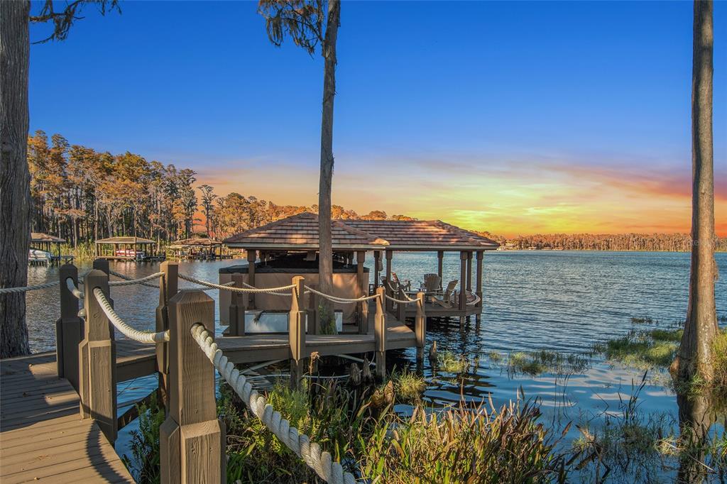 A wooden dock with a covered boat slip extends into a lake at sunset — 9349 TIBET POINTE CIRCLE, WINDERMERE, FL