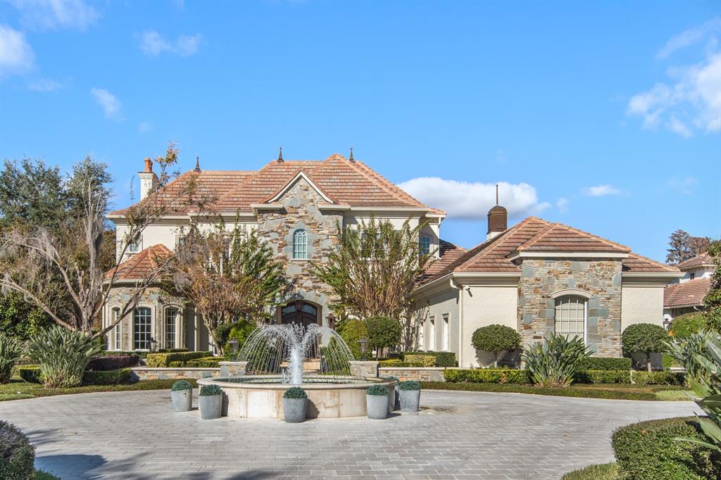A large stone and stucco house with a tile roof and a circular fountain driveway — 9349 TIBET POINTE CIRCLE, WINDERMERE, FL