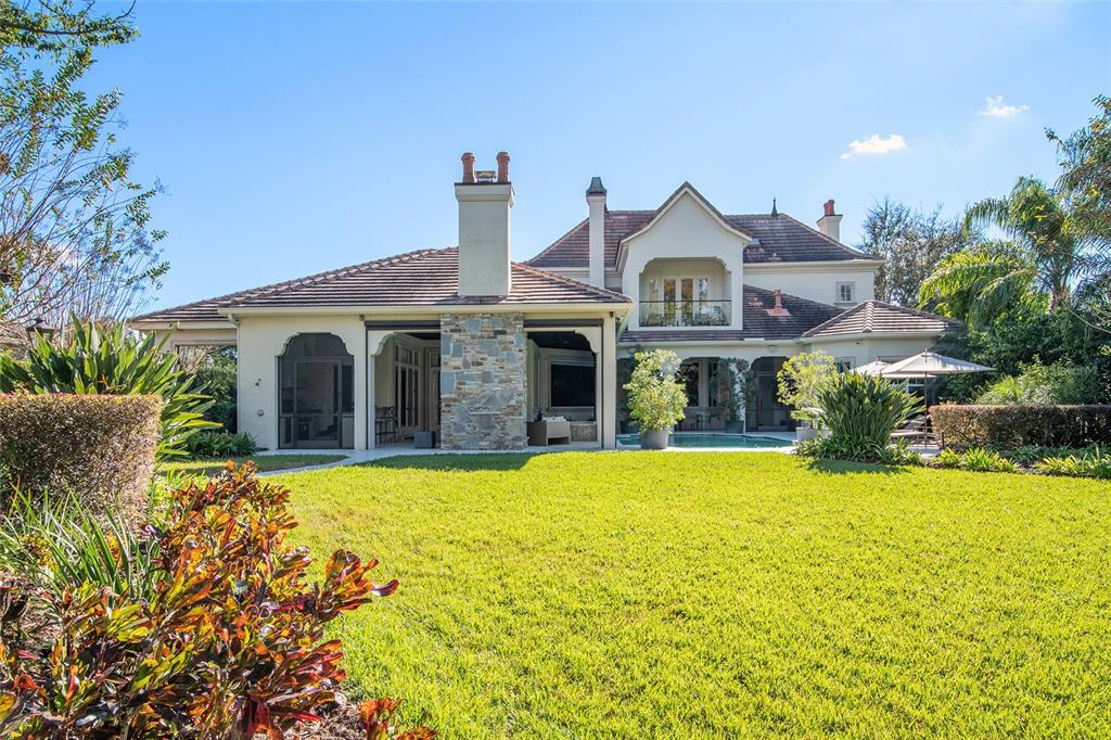 The rear exterior of a two-story house features a stone chimney, pool, and lawn — 9349 TIBET POINTE CIRCLE, WINDERMERE, FL