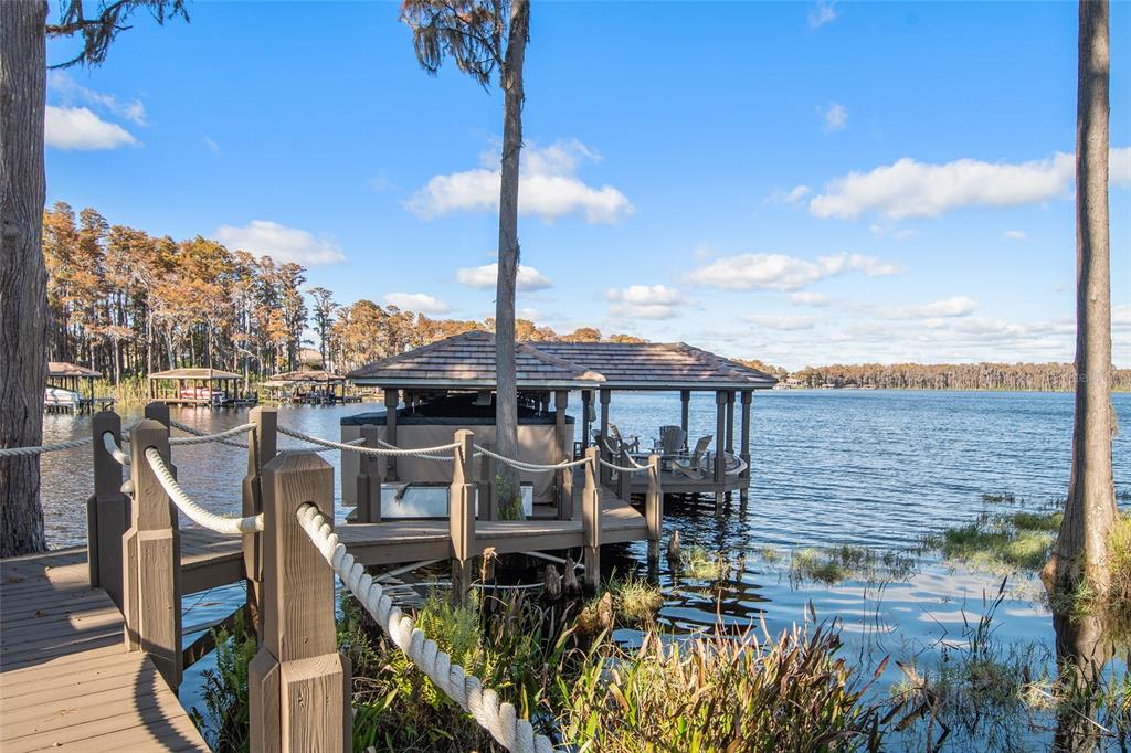 A wooden dock leads to a covered boat slip on a lake with cypress trees — 9349 TIBET POINTE CIRCLE, WINDERMERE, FL