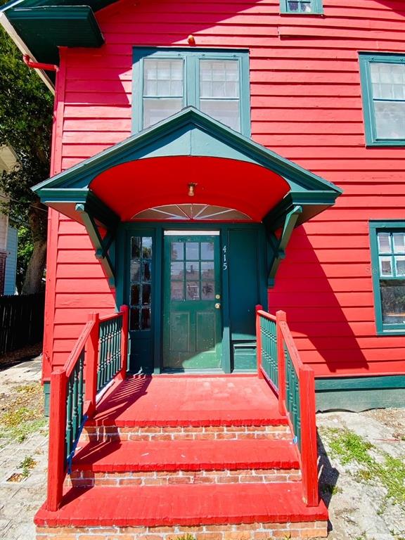 A red house exterior features a green-trimmed front door under a matching gabled porch roof — 415 BRADDOCK AVENUE, DAYTONA BEACH, FL