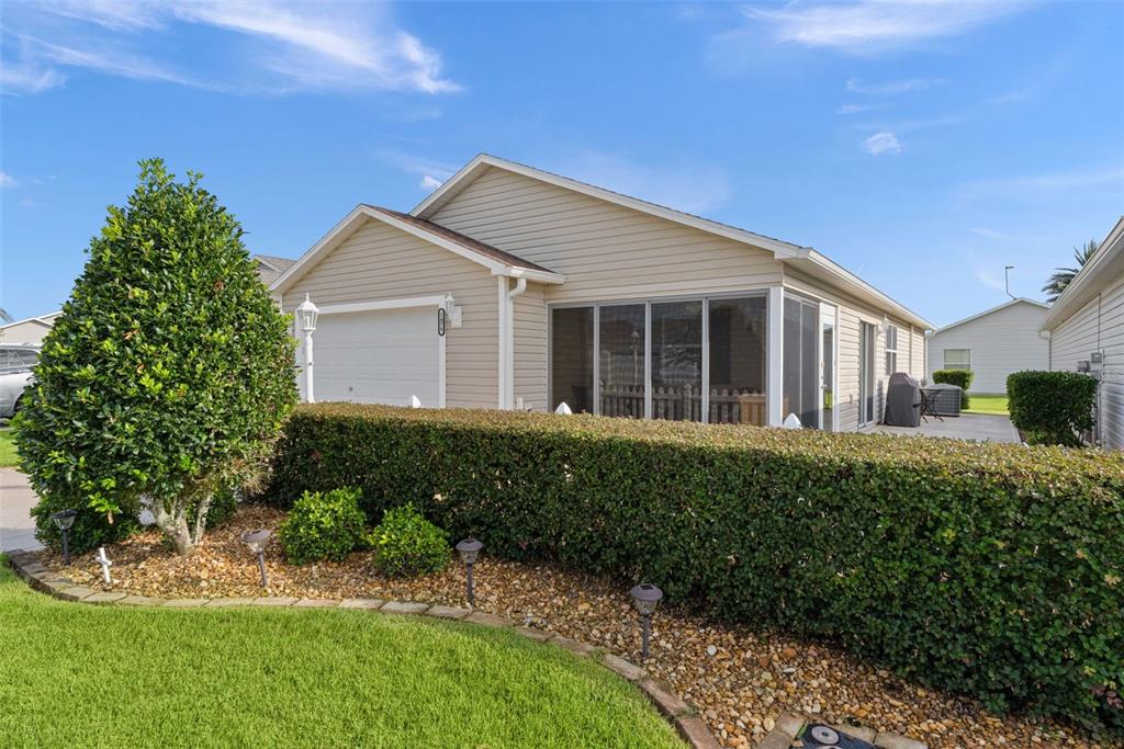 A beige house with a garage, a screened-in porch, and a manicured hedge in front — 1479 OLYMPIA STREET, THE VILLAGES, FL