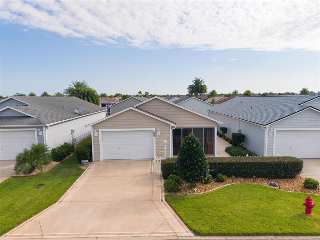 An exterior view of a tan, single-story house with a two-car garage and landscaped yard — 1479 OLYMPIA STREET, THE VILLAGES, FL