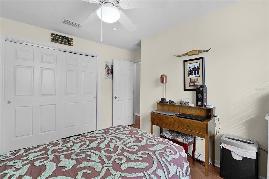 A bedroom features a bed with a patterned quilt, a wooden desk, and white closet doors — 1479 OLYMPIA STREET, THE VILLAGES, FL