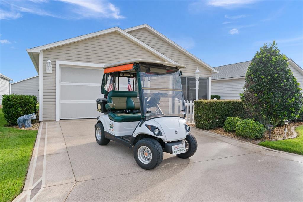 A white golf cart is parked on the concrete driveway in front of a suburban house — 1479 OLYMPIA STREET, THE VILLAGES, FL
