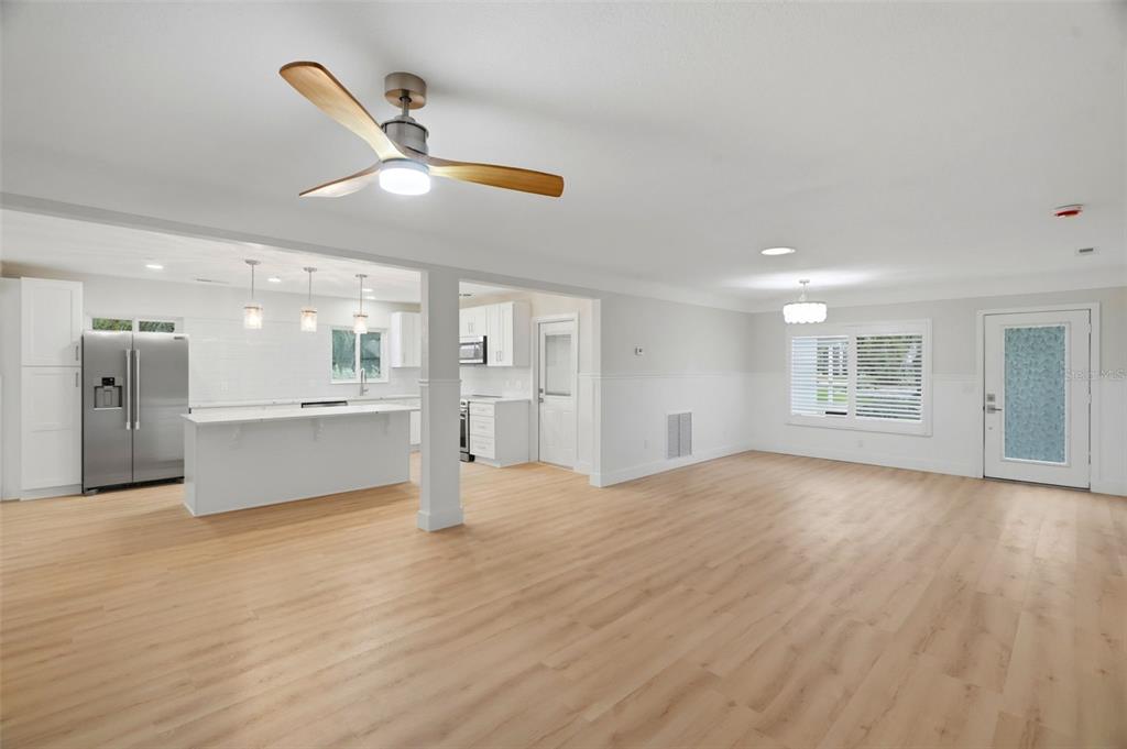An open-concept kitchen and living area features light wood flooring, white cabinetry, and a ceiling fan — 15814 3RD STREET E, REDINGTON BEACH, FL