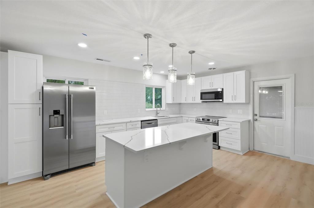 A modern kitchen features white cabinetry, stainless steel appliances, a quartz island, and light wood flooring — 15814 3RD STREET E, REDINGTON BEACH, FL