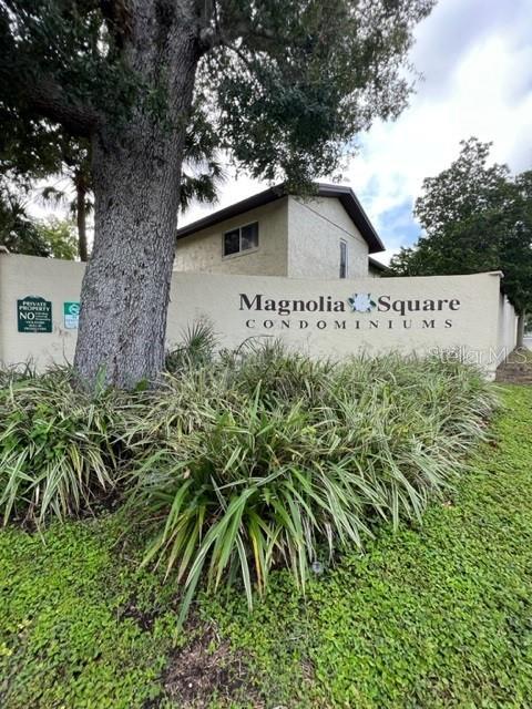 A large tree stands in front of a beige wall sign for Magnolia Square Condominiums — 501 E BAY DRIVE UNIT 104, LARGO, FL