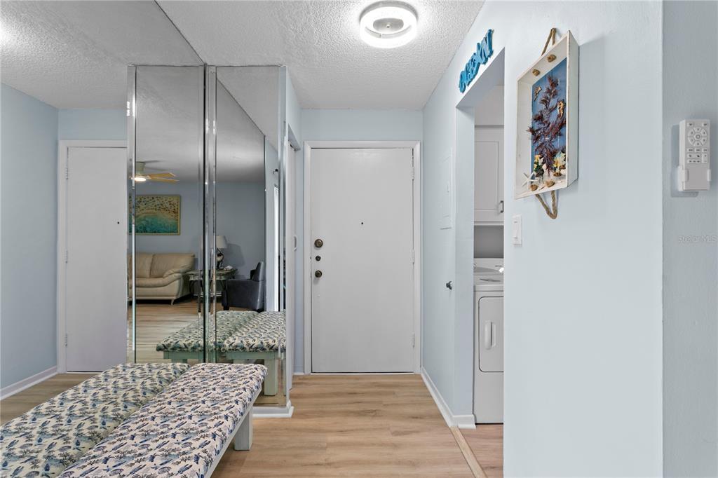 An entryway features light wood flooring, mirrored closet doors, a patterned bench, and a white door — 501 E BAY DRIVE UNIT 104, LARGO, FL