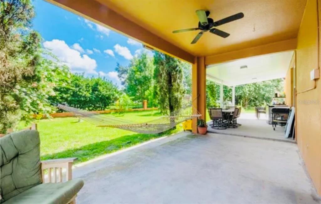 A covered patio features a ceiling fan, a hammock, and a view of the backyard — 13315 DAFFODIL WAY, ASTATULA, FL