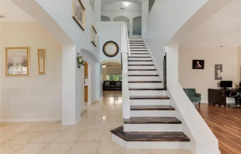 A bright entryway features a tiled floor, a wooden staircase, and a view into another room — 13315 DAFFODIL WAY, ASTATULA, FL