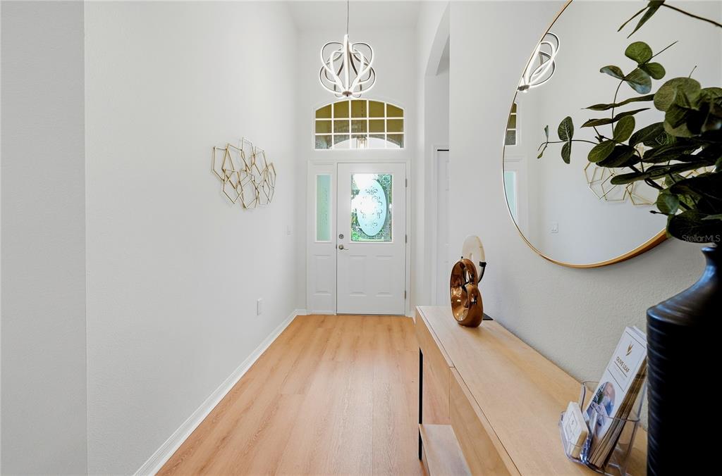 A bright entryway features light wood flooring, a modern chandelier, and a console table — 6817 SUPERIOR STREET CIRCLE, SARASOTA, FL