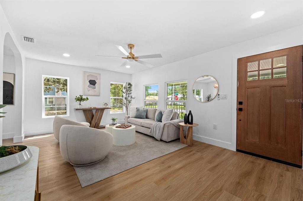 A living room features light wood flooring, a beige sofa, two armchairs, and a wooden door — 1230 E HENRY AVENUE, TAMPA, FL