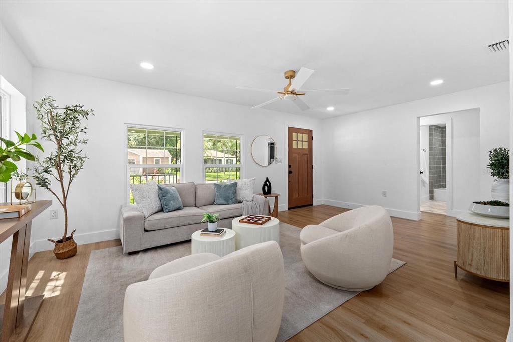A bright living room features a grey sofa, two cream armchairs, and light wood flooring — 1230 E HENRY AVENUE, TAMPA, FL