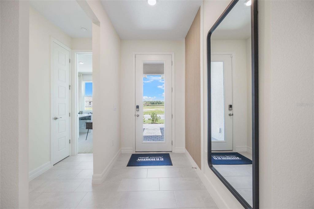 A bright entryway features light tile flooring, a front door, and a large wall mirror — 3952 KENNEBUNK LOOP, MOUNT DORA, FL