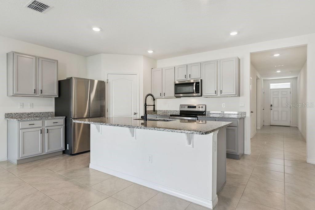 A kitchen features gray cabinets, granite countertops, a central island, and stainless steel appliances — 5235 MAHOGANY DRIVE, MOUNT DORA, FL