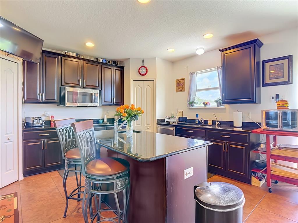 A kitchen features dark wood cabinets, granite countertops, a center island, and tile flooring — 205 TIFTON STREET, WINTER HAVEN, FL