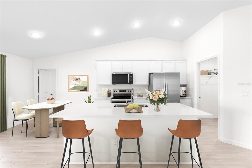 A modern kitchen features white cabinetry, a large central island with bar seating, and stainless appliances — 3510 E ELIAS CIRCLE, NORTH PORT, FL