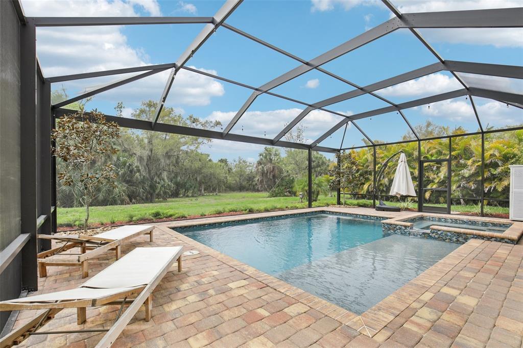 A screened-in pool patio features a spa, paver deck, and lounge chairs overlooking a yard — 20604 BENISSIMO DRIVE, VENICE, FL