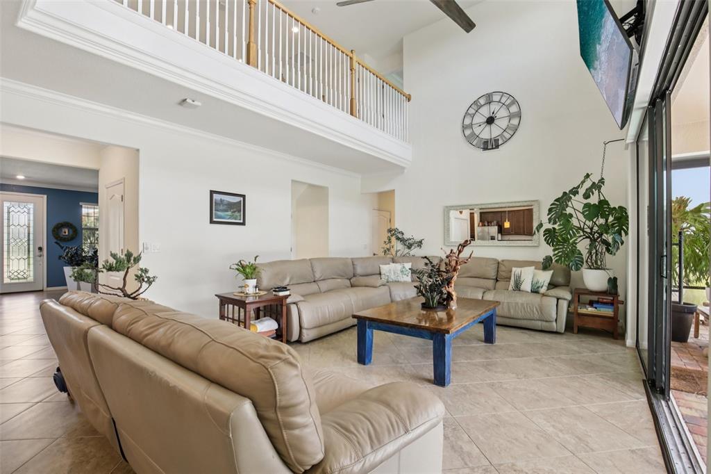 A spacious living room features a high ceiling, a large sectional sofa, and a balcony overlook — 20604 BENISSIMO DRIVE, VENICE, FL