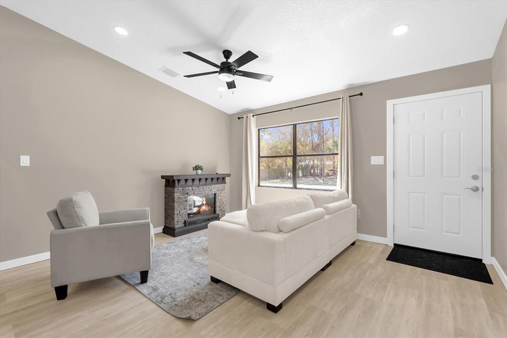 A living room features a stone fireplace, a white sofa, an armchair, and light flooring — 4840 MANGO AVENUE, COCOA, FL