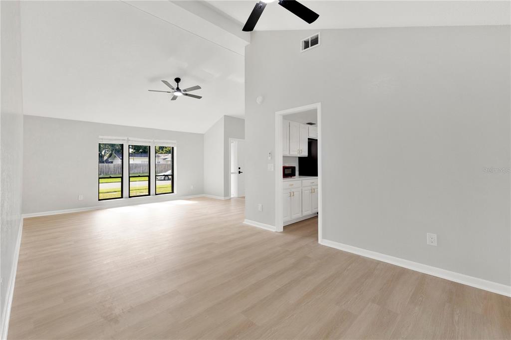 A bright living room features light wood-look flooring, vaulted ceilings, and a doorway to a kitchen — 5313 JADE CIRCLE, BELLE ISLE, FL