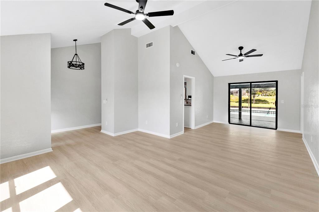 An empty living room features light wood-look flooring, vaulted ceilings, two ceiling fans, and sliding doors — 5313 JADE CIRCLE, BELLE ISLE, FL