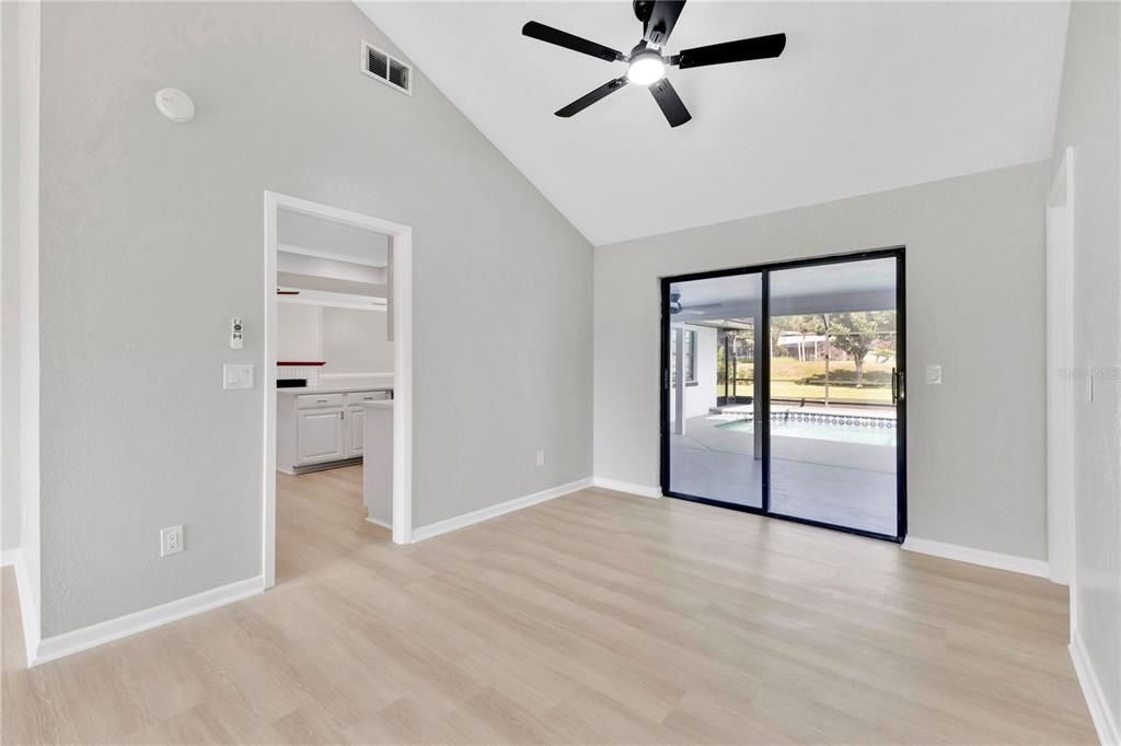 A living room with light wood flooring, a vaulted ceiling, and sliding glass doors to a pool — 5313 JADE CIRCLE, BELLE ISLE, FL