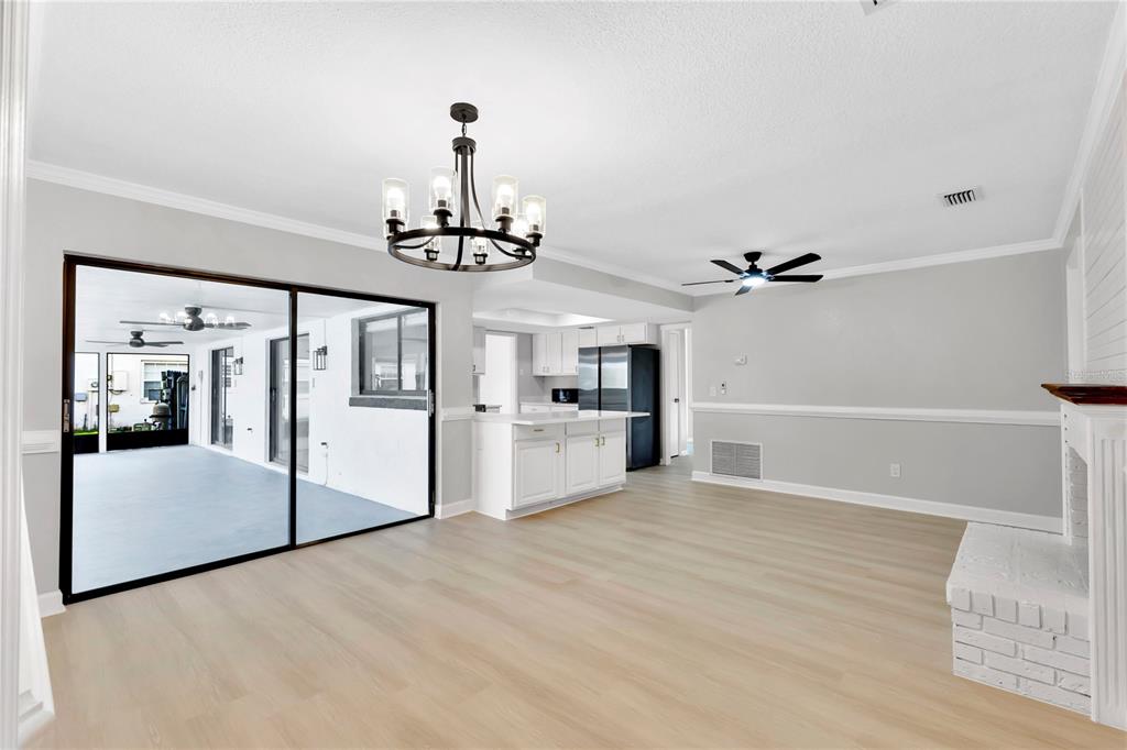 A bright living room with light wood floors, a chandelier, and a sliding glass door — 5313 JADE CIRCLE, BELLE ISLE, FL