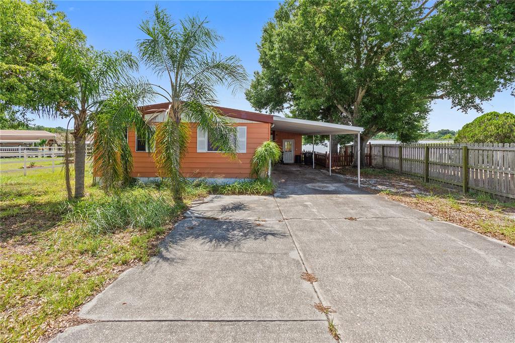 A single-story orange house with a concrete driveway, carport, and palm trees in the yard — 1025 CARVER STREET, LAKE WALES, FL