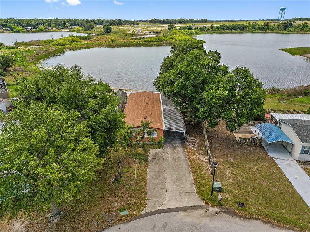 An aerial view shows a single-story home with a carport situated beside a large lake — 1025 CARVER STREET, LAKE WALES, FL