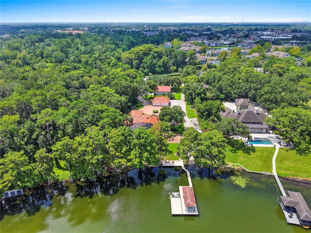 An aerial view of a waterfront property featuring two houses, docks, and dense surrounding trees — 2622 LAKE HOWELL LANE, WINTER PARK, FL