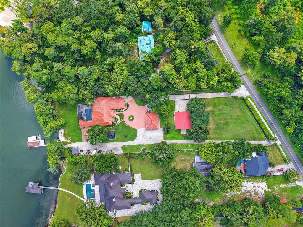 Aerial view of two waterfront houses with pools, docks, and large wooded lots near a road — 2622 LAKE HOWELL LANE, WINTER PARK, FL