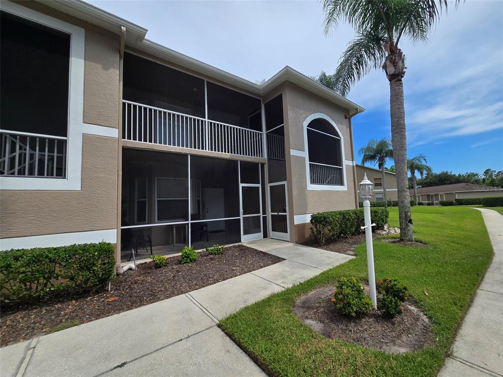 A two-story building exterior features a screened-in patio, a white railing, and a palm tree — 5320 HYLAND HILLS AVENUE UNIT 2218, SARASOTA, FL