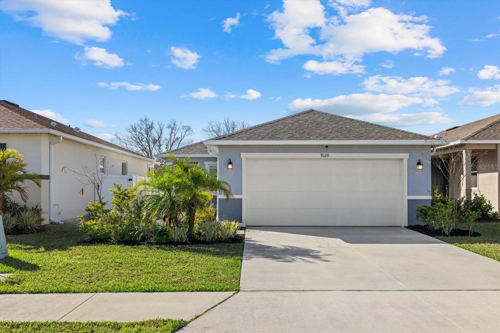 A single-story house with a two-car garage and a concrete driveway under a blue sky — 9120 SANDY BLUFFS CIRCLE, PARRISH, FL